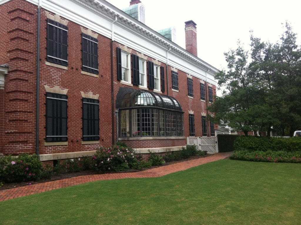 - american hurricane shutters A stately red brick building with hurricane shutters near rounded glass-paned bay windows.