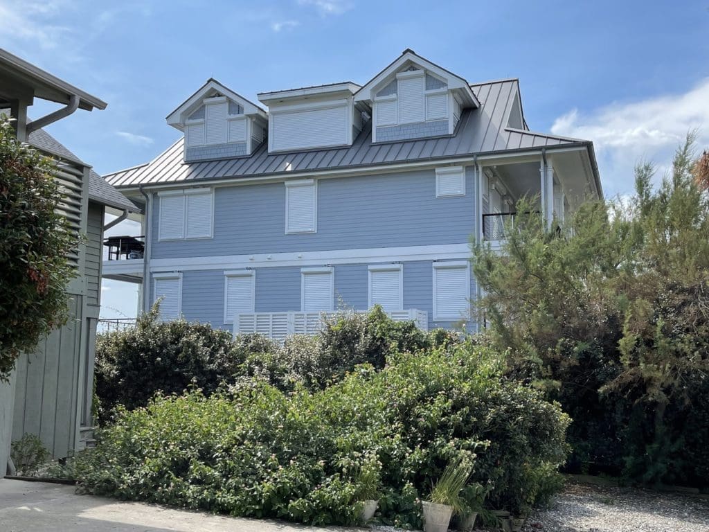 Sunny topsail coastal home with white hurricane shutters - american hurricane shutters Topsail blue coastal home, white hurricane shutters, dark metal roof.
