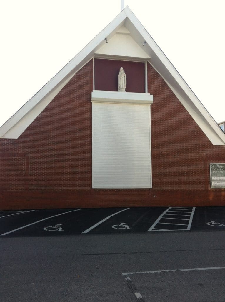 Wilmington brick church: storm panels protect statue - american hurricane shutters Red brick church: white statue protected by storm panels.