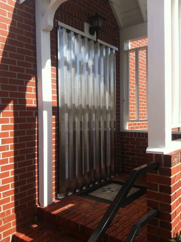 - american hurricane shutters Aluminum hurricane panels installed on a brick home entrance, demonstrating storm protection solutions for homeowners.