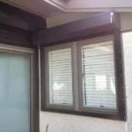 Exterior wall with two windows: a sliding glass door on the left and a small window with closed blinds on the right, framed in dark material against a light-textured wall. in either North or South Carolina