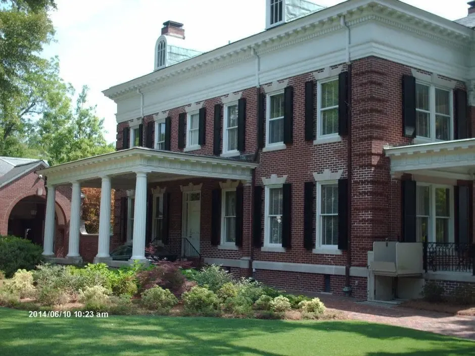 Colonial-style house with white columns, black shutters, and landscaped garden, showcasing traditional architecture and potential for hurricane protection solutions.
