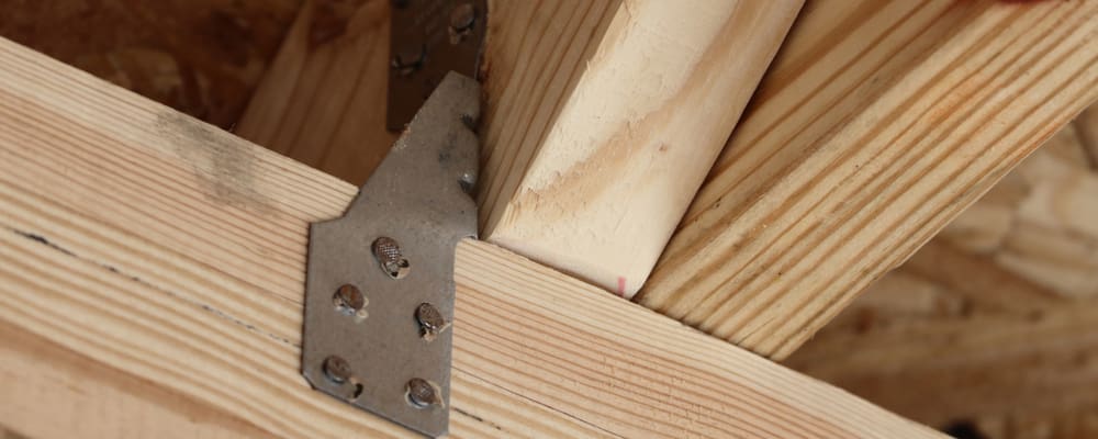 Close-up of a wooden beam joint reinforced with a metal bracket, showcasing Wilmington residents' preferred storm protection solutions. The bracket is secured with screws, connecting two angled beams in a construction setting. Wood grain and textures are visible, highlighting the sturdiness of the structure. in either North or South Carolina