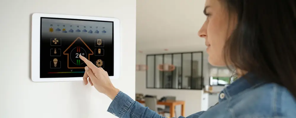 A Wilmington homeowner uses a smart home control panel mounted on the wall, adjusting the temperature to 24°C. The screen displays home climate icons and weather forecasts. The modern interior background features sleek designs and electric rolldown shutters, highlighting top trends in smart living. in either North or South Carolina