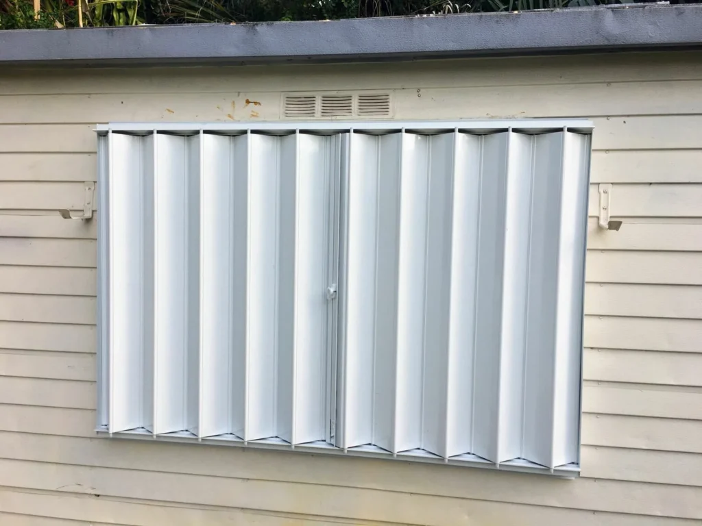 Accordion hurricane shutters closed on a window, showcasing their durable design and rust-proof materials, ideal for storm protection in coastal areas like Myrtle Beach.