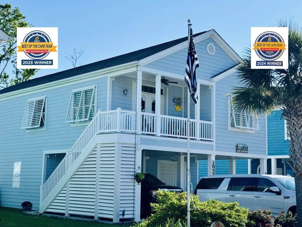 A light blue two-story house with white trim, hurricane shutters, and a front porch, an American flag, a white SUV parked outside, and "Best of the Cape Fear" 2023 and 2024 award badges displayed in the corners. in either North or South Carolina - American Hurricane Shutters A light blue two-story house with white trim, hurricane shutters, and a front porch, an American flag, a white SUV parked outside, and "Best of the Cape Fear" 2023 and 2024 award badges displayed in the corners. in either North or South Carolina